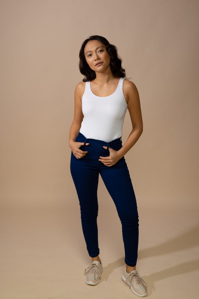 Asian woman with dark hair standing with thumbs in belt loops, copy space