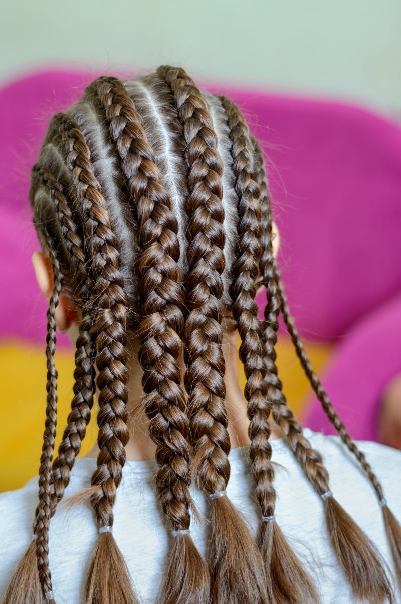 The girl demonstrates her hairstyle with afro-braids. Rear view. Vertical view. Selective focus.